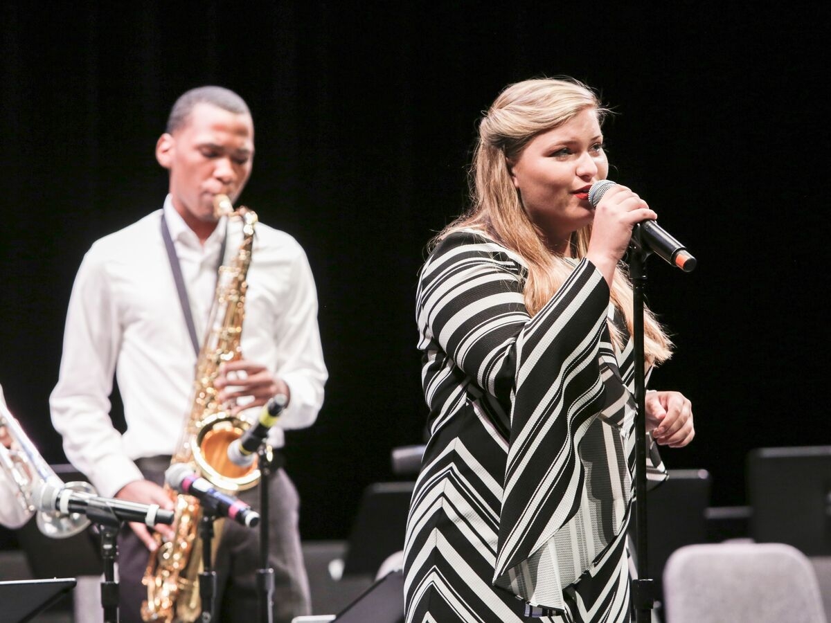 A vocalist and saxophone player perform on stage