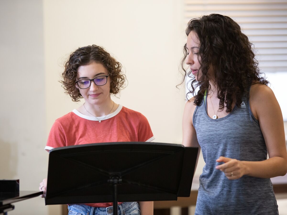 A singer and their instructor discuss music while looking at the music stand