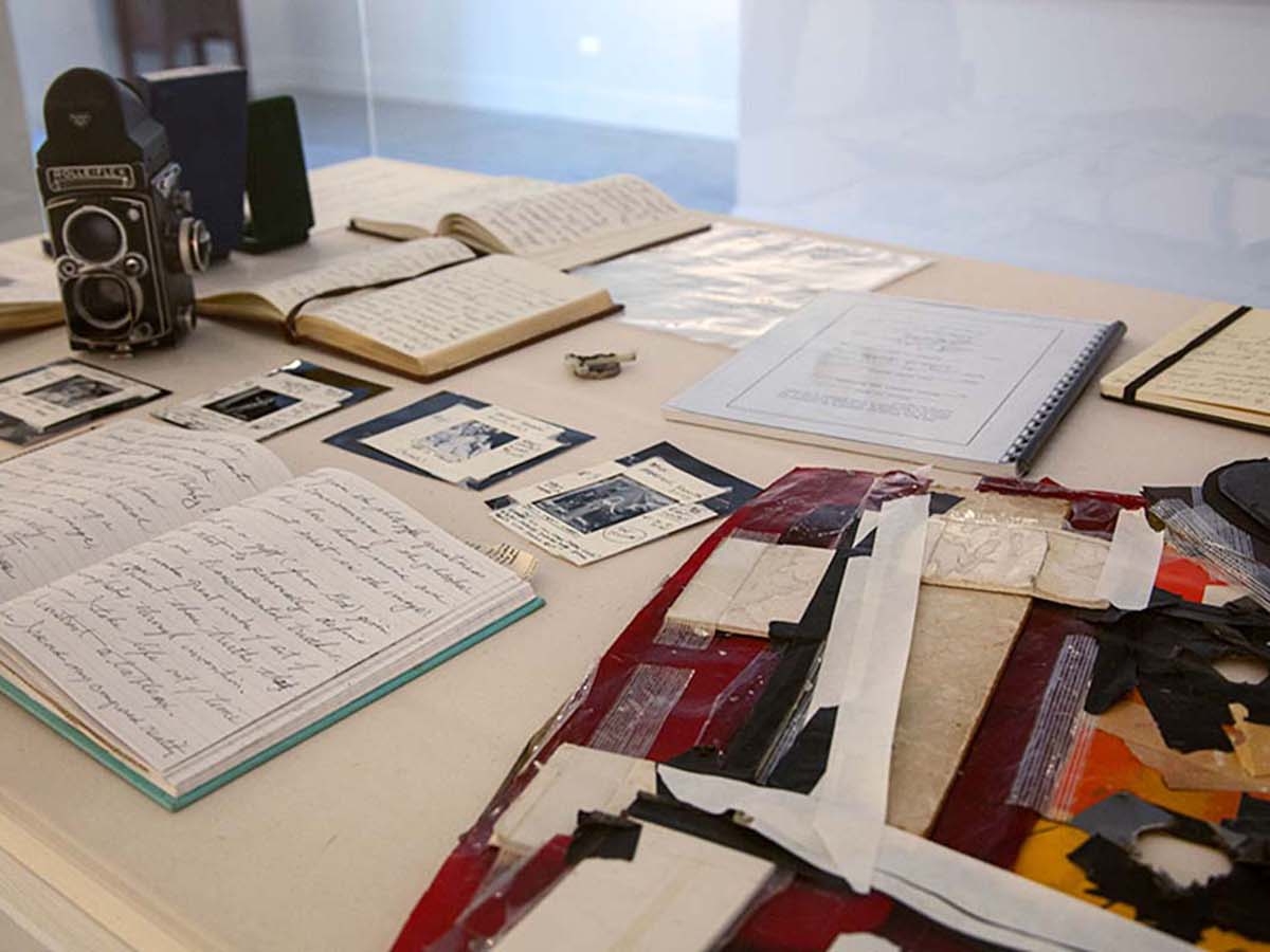 Detail view from installation of Joel-peter Witkin: From The Studio at Catherine Edelman Gallery. Photography equipment, scraps of paper, open notebooks and photographs with handwritten notes are displayed on a table in the gallery space.