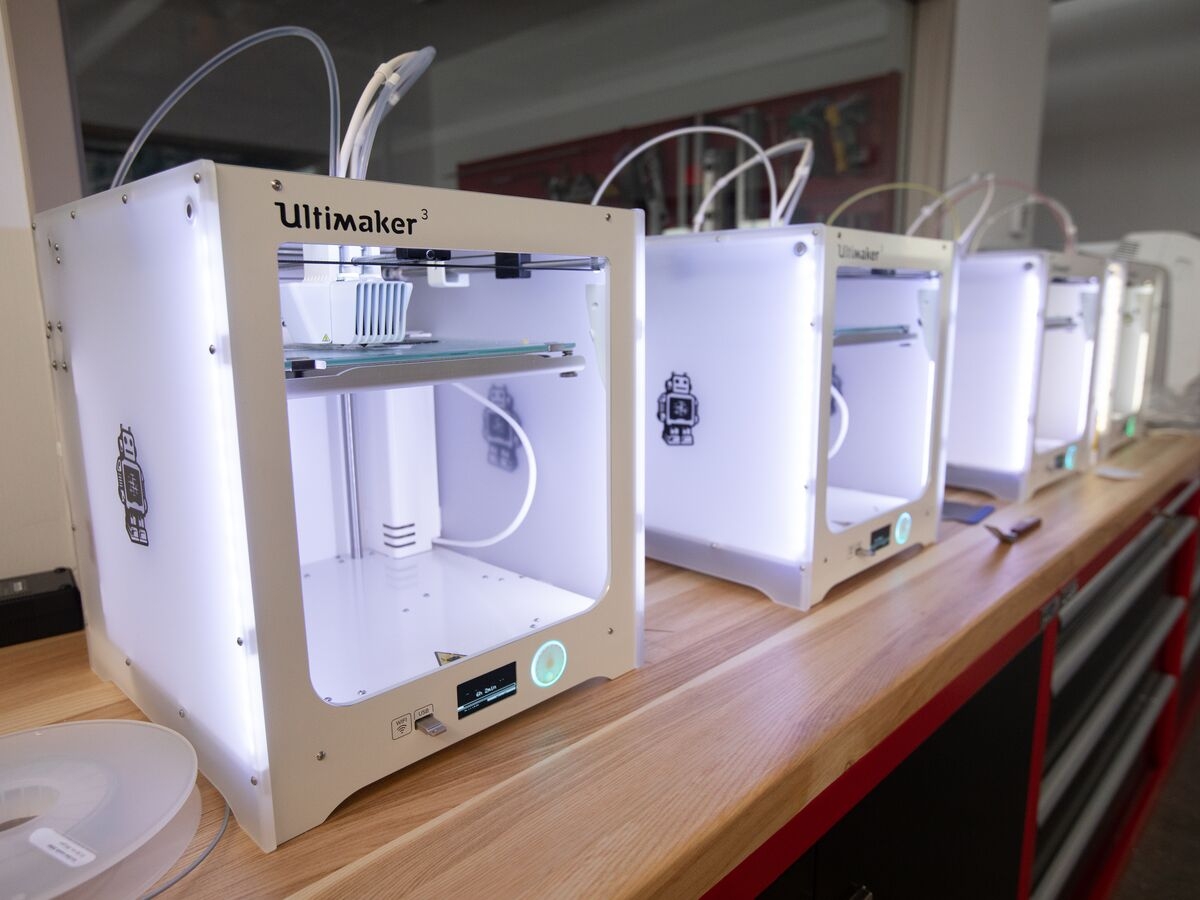 a row of four white 3D printers in the UArts makerspace. they are powered on and glowing 