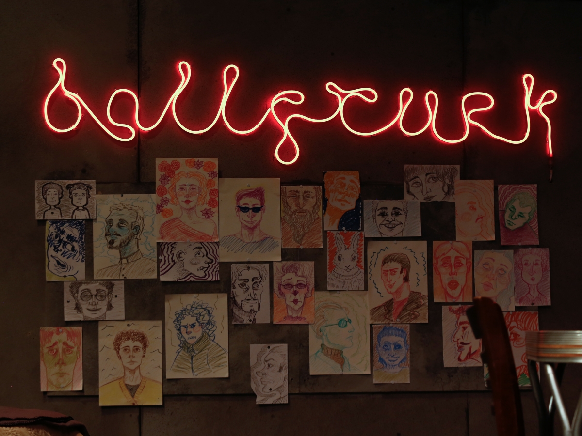 still of ballyturk stage. ballyturk is written in squiggly red neon-like strip above a wall of colorful drawn portraits.