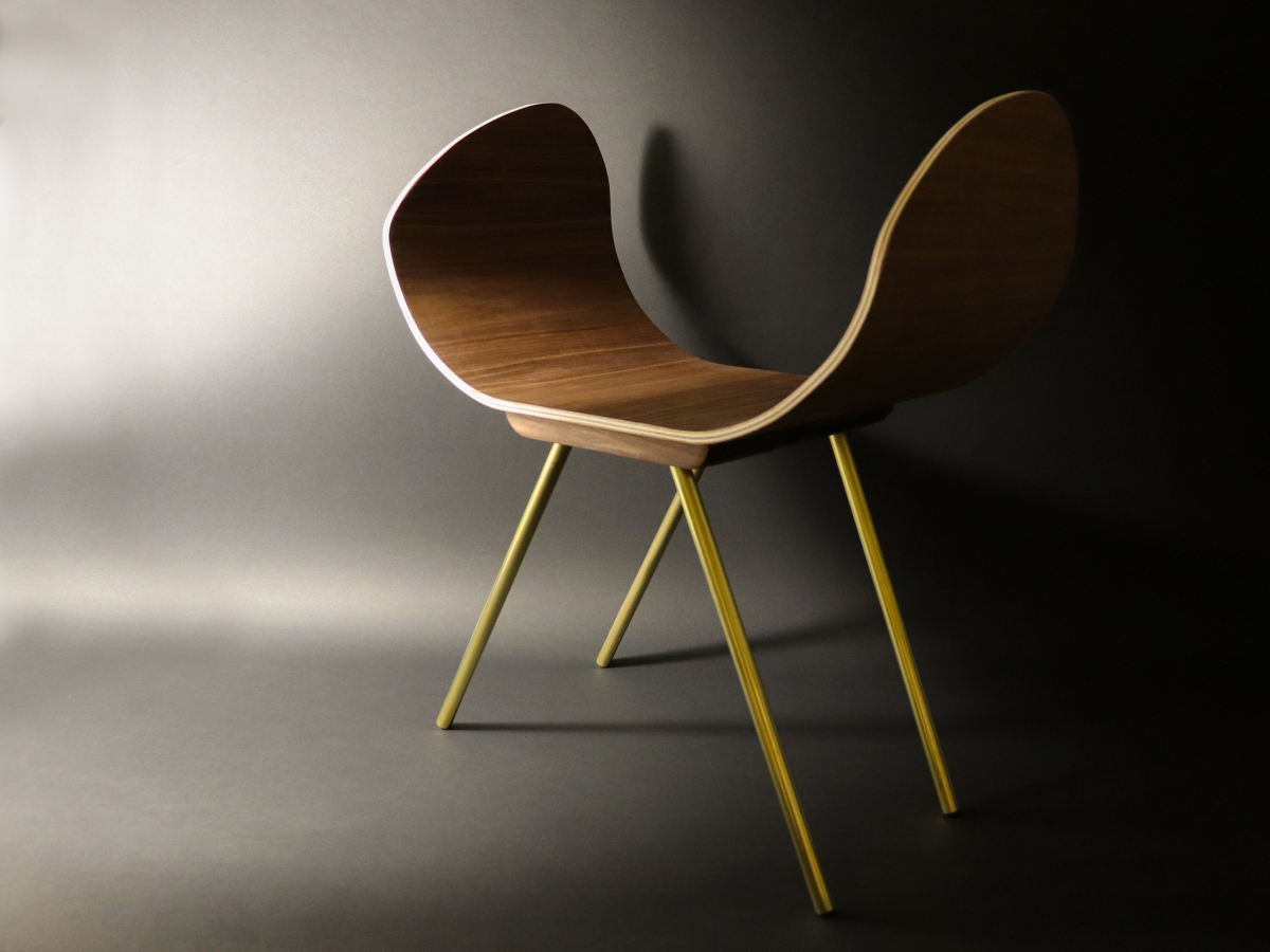 The image appears to be a 3d rendering but it could just as easily be a minimal photograph. A curved seat rendered in a warm wood grain is set atop four brass-like legs diagonally angled below its base. The overall shape of the furniture is inviting.
