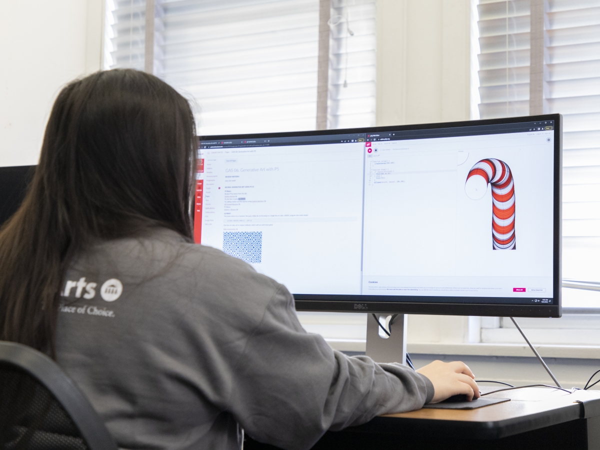 A student sits at a widescreen monitor with a worm-like shape on one side of the screen.