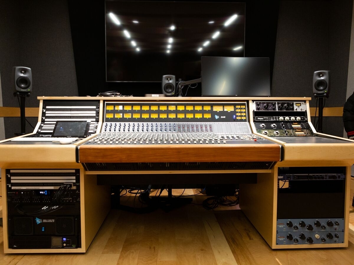 A recording and mixing studio setup, with a large mixing console in the center of a large wooden mixing desk. There are patchbays on the left desk panels and outboard rack-mounted equipment on the right panels. The desk is trimmed in light wood.