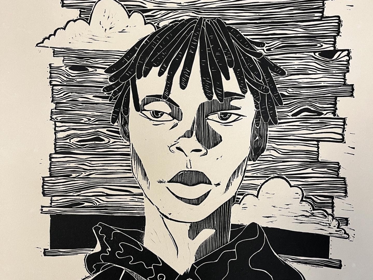 a linocut of a person with a black hoodie and short dreaded hair pictured against a sky with clouds, rendered as if the sky is formed by planks of wood. 