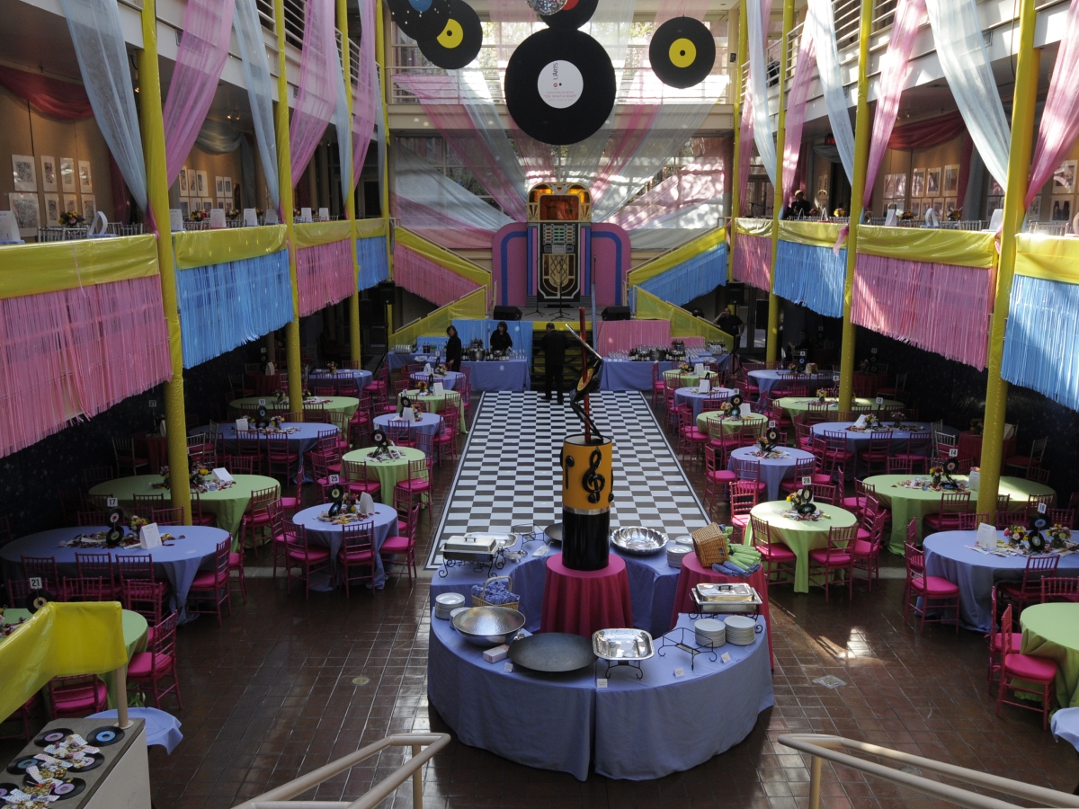 solmssen court decorate for a music-themed event in pastel colors. giant faux vinyl records hang from the ceiling as the cross stairwells across from CBS auditorium are decorated to resemble a jukebox. dining tables are in pastel violet, green colors with red and pink accents, as long streamers and drapes in blue, pink, and white cover the space. 