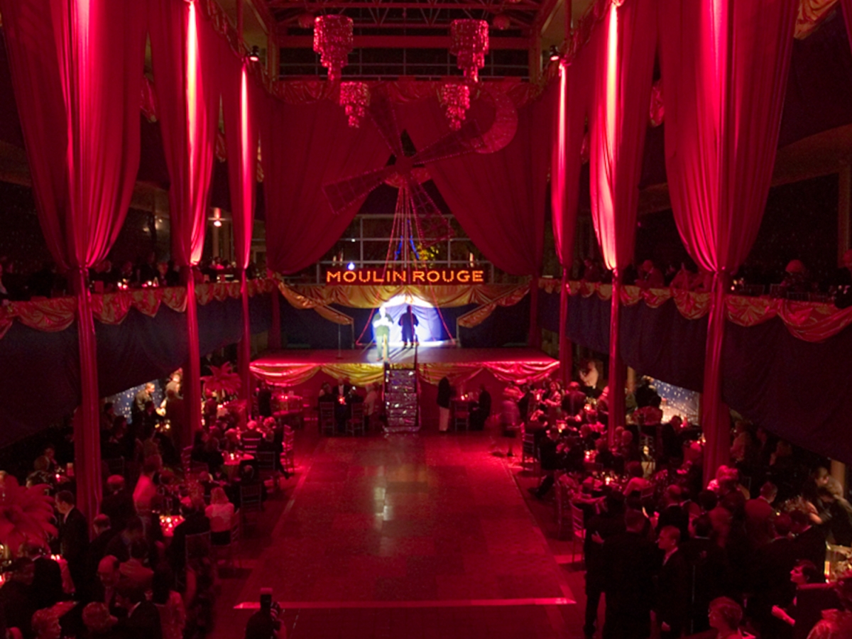interior of solmssen court decorated in a moulin rouge theme. large drapes hang along the three stories of pillars, highlighted with crimson light. 