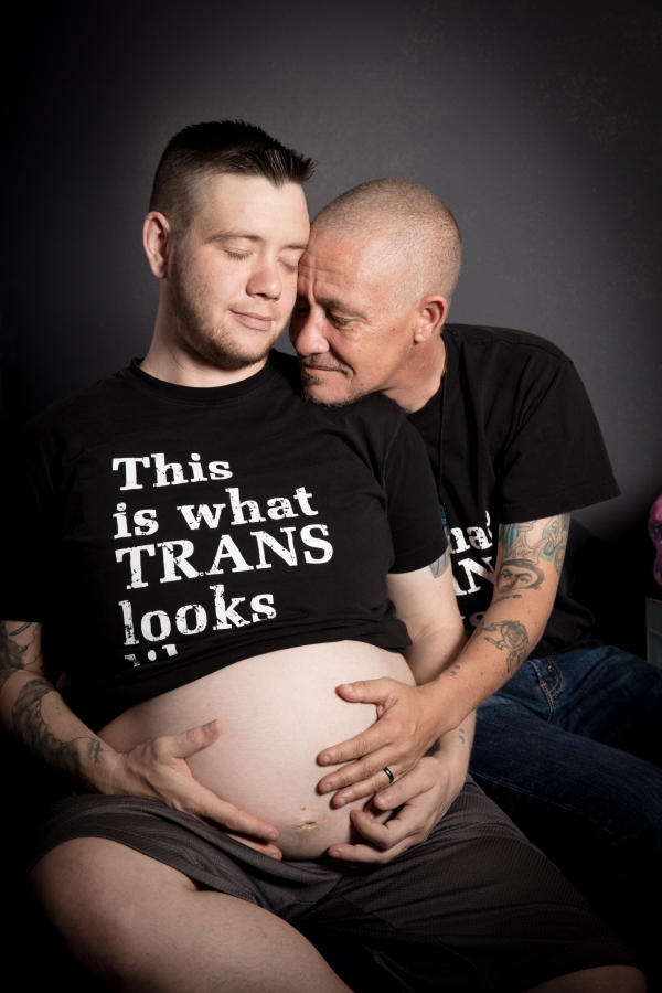 A trans couple with their eyes closed and holding each other with one person pregnant