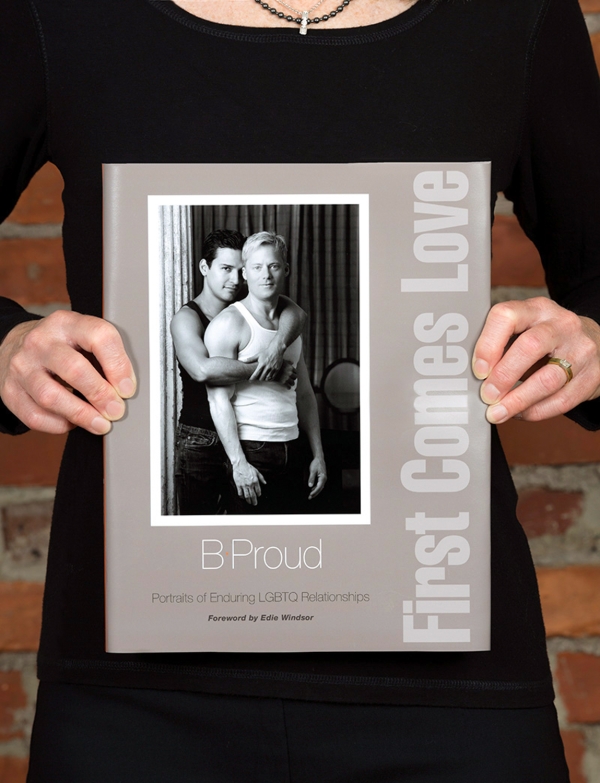A closeup of B. Proud holding her book First Comes Love which has a black and white photo on it and the title running vertically up the right side
