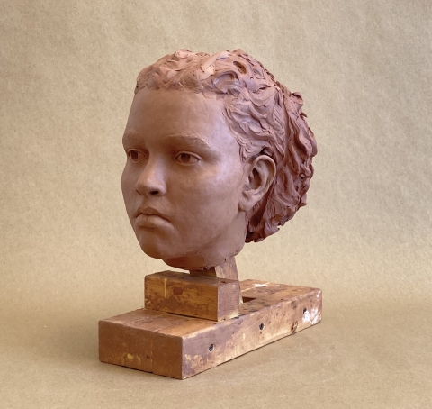 sculpture by lola smith. a clay head is shown at 3:4 angle with a slight frown and wavy hair tied back