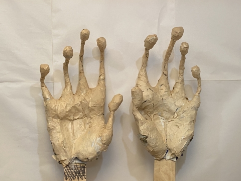 sculpture by lola smith. two spindly, surreal hands with large bulbs at the end of each finger, like papier mache frog hands. 