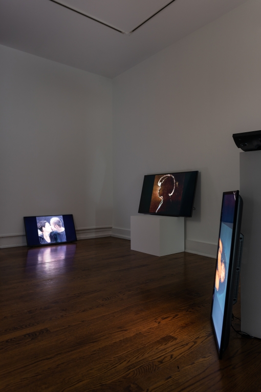 an installation shot of Abbey Williams' work in a gallery space. Three digital monitors are around the room leaning against and on top of pillars. The screens displaying stills from various videos each featuring a different female figure shown.