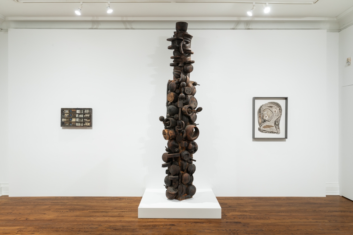 three works are installed in a gallery space. Two 2-d Works hang along the back wall. A tall sculptural works in the foreground is situated between the other two works pictured. 