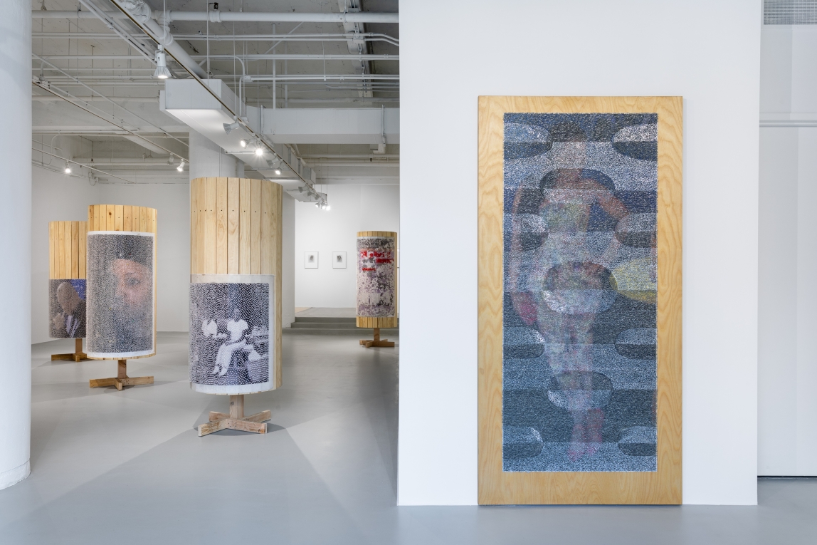 Installation view with large floor length wall work in right foreground, wooden columns with images in background