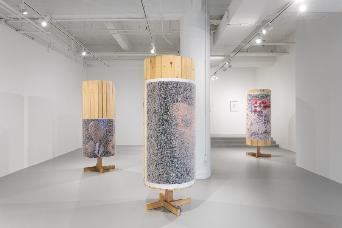 Installation view of wooden columns with posters covered in tacks