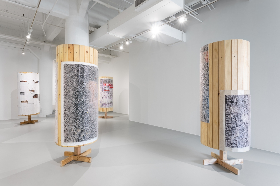 Installation view of wooden column works covered in posters, some covered in tacks
