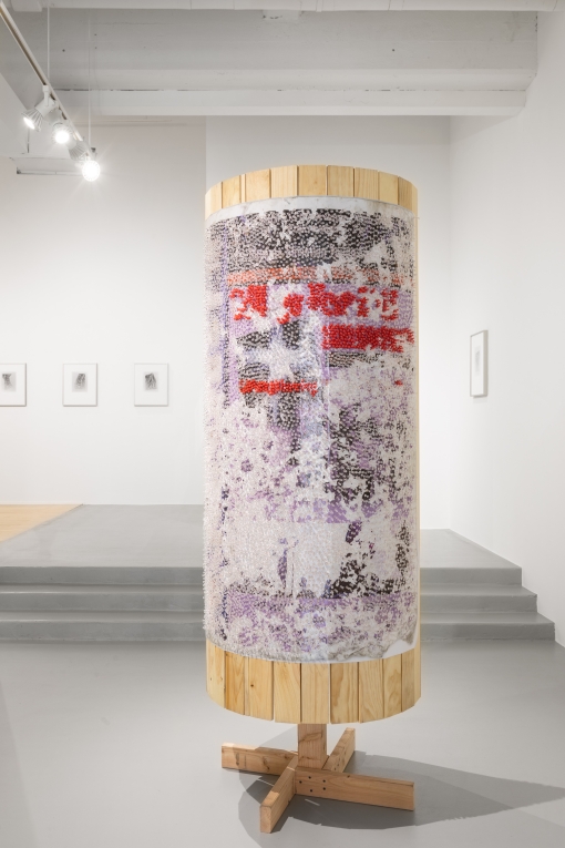 Installation view of one wooden column with poster covered in clear and red tacks