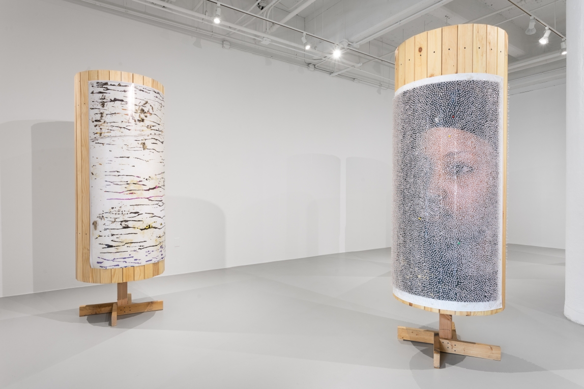 Installation view of two wooden columns with posters covered in tacks
