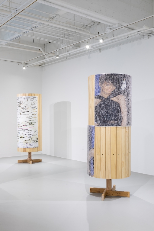 Another installation view of two wooden columns, showing a different angle and images on said columns