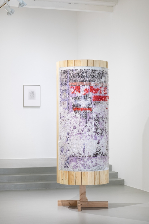 Image of single wooden column with poster covered in red and clear tacks with one framed work on background wall