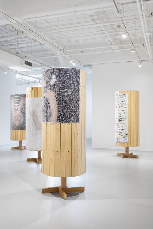 Installation view of four wooden columns covered in posters and tacks