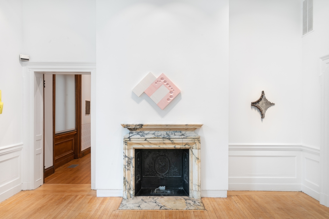 Installation image of two wall sculptures, one made of metal, the other plaster