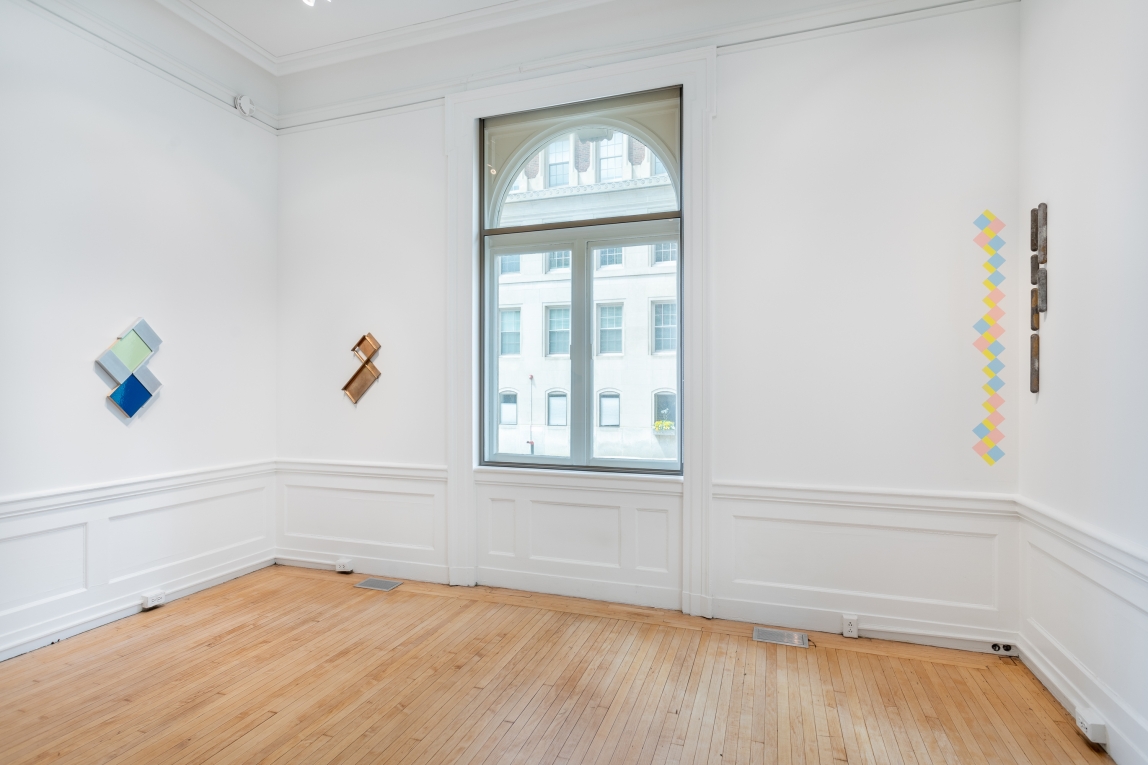 Three sculpture works on view inside of a white room with a window; one is made of plaster/casting and metal; the second is made of metal and the third consists of metal and wall adhesives