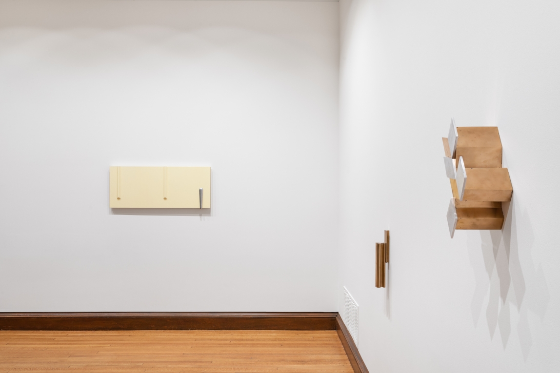 installation view of adjoining walls with three sculptures on display: yellow cast sculpture in background, two metal compositions in right foreground