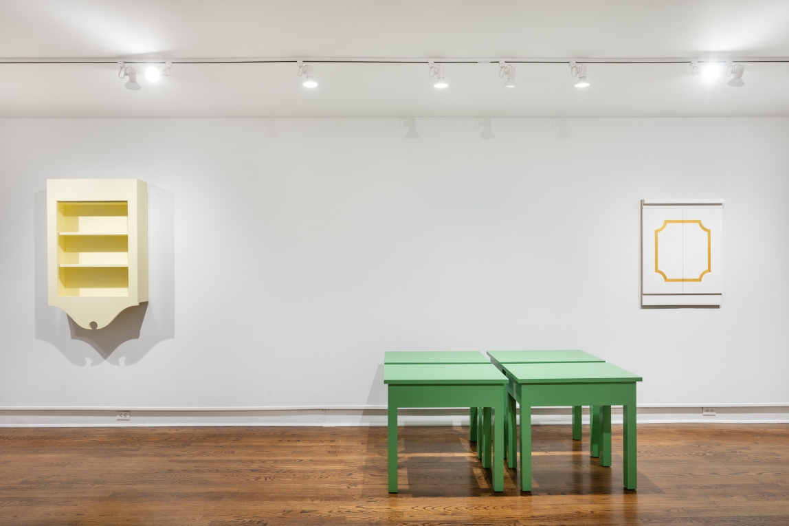 Installation view of a yellow hanging cabinet, hanging white doors with gold trim and four green tables grouped together