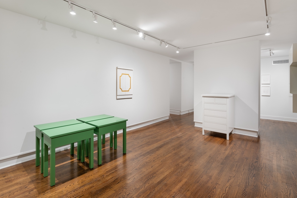 Installation view with four green tables grouped to the left, cabinet doors hanging in background and a white chest of drawers to the right