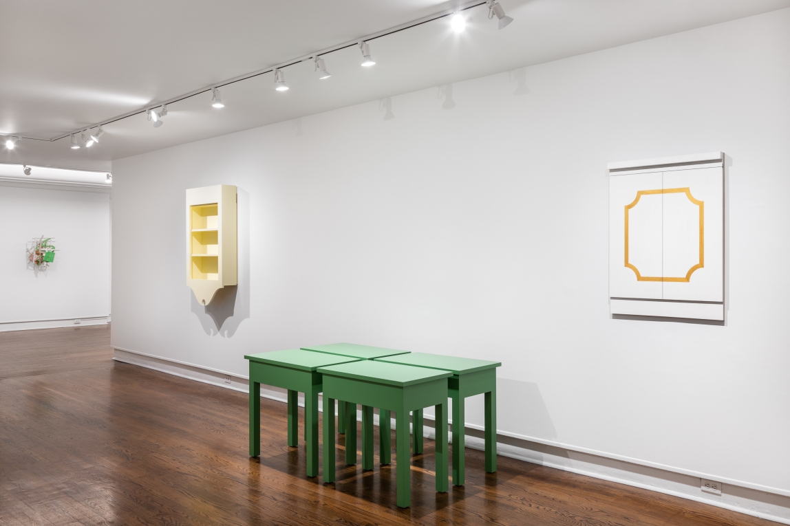 Installation view with yellow hanging cabinet in background, four green tables grouped together in center and white hanging doors in right foreground