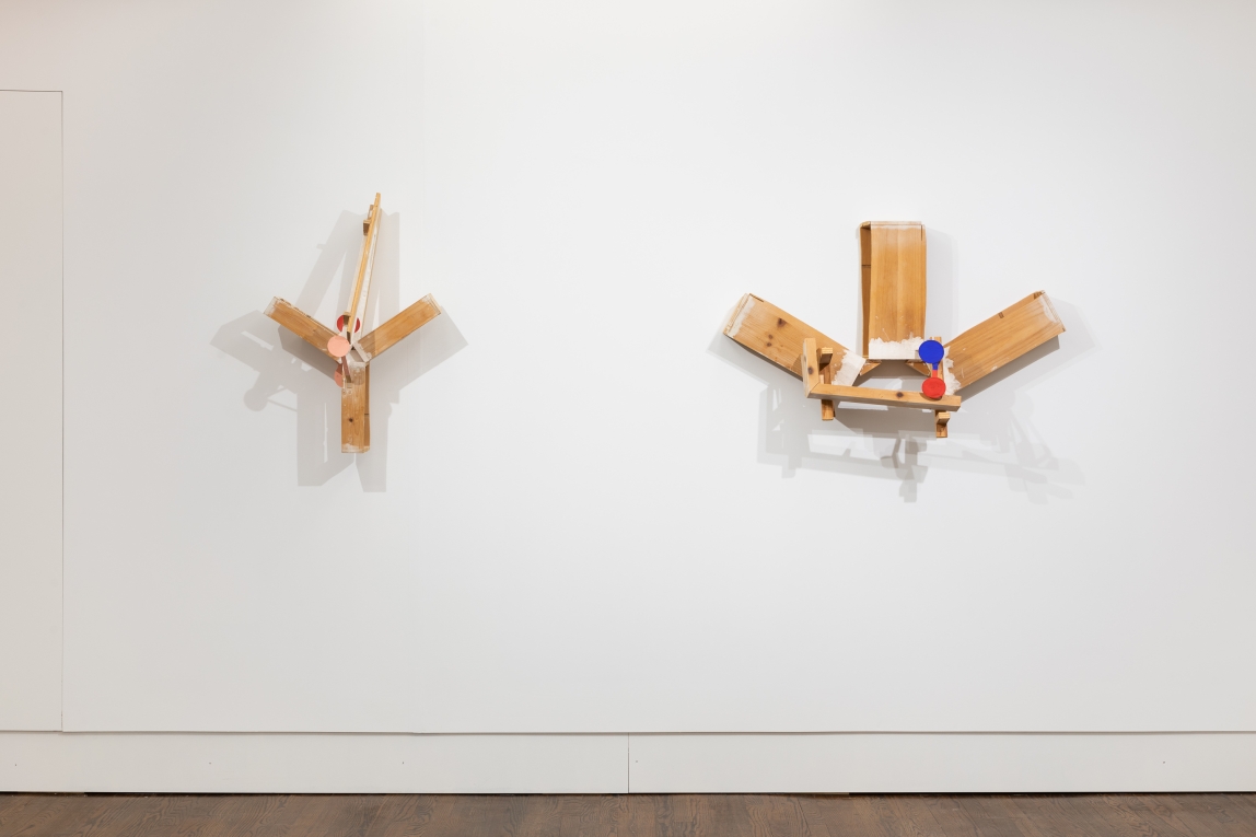 Installation of two wall sculptures hanging side by side consisting of wood arranged in y or sun shape