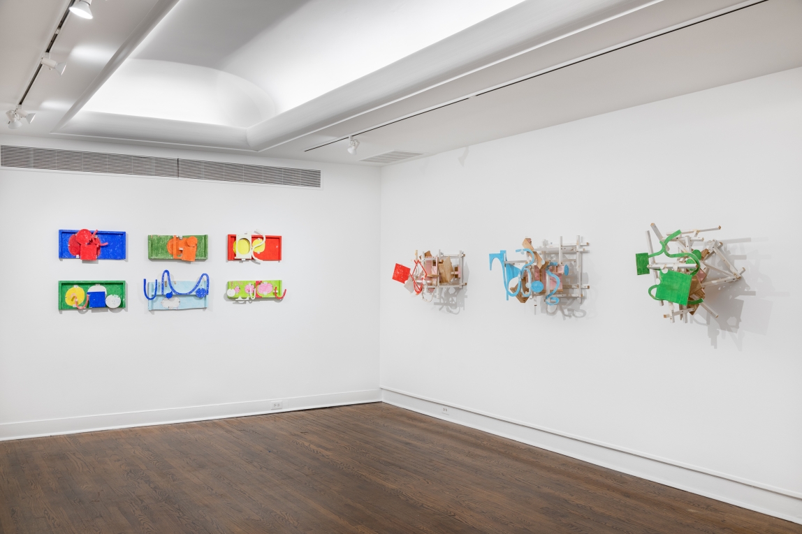 Installation view with a wall of flater wood sculptures to the left and a wall of assembled 3D wood sculptures to the right