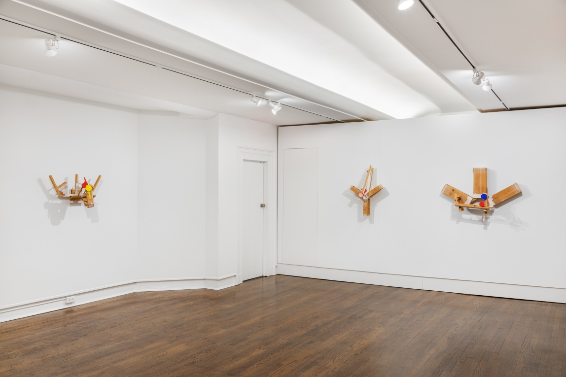 Installation view of three wood and raised sculptures hanging on the wall, one to the left and two to the right