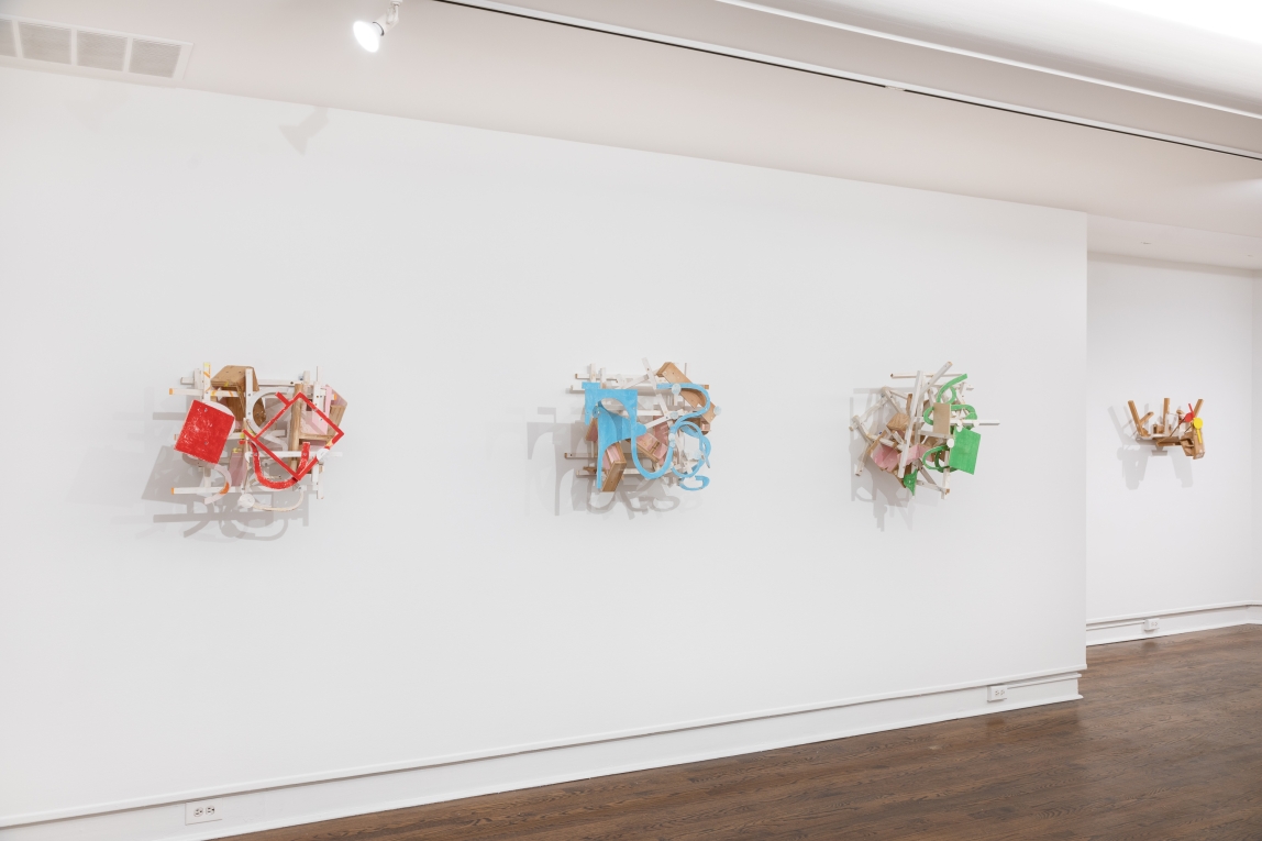 Installation view of wall with raised wood sculptures hanging in a row across it