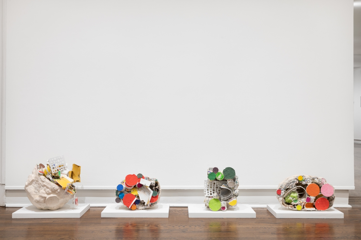 Installation view of four colorful sculptures composing of found materials  lined up in a row on the floor