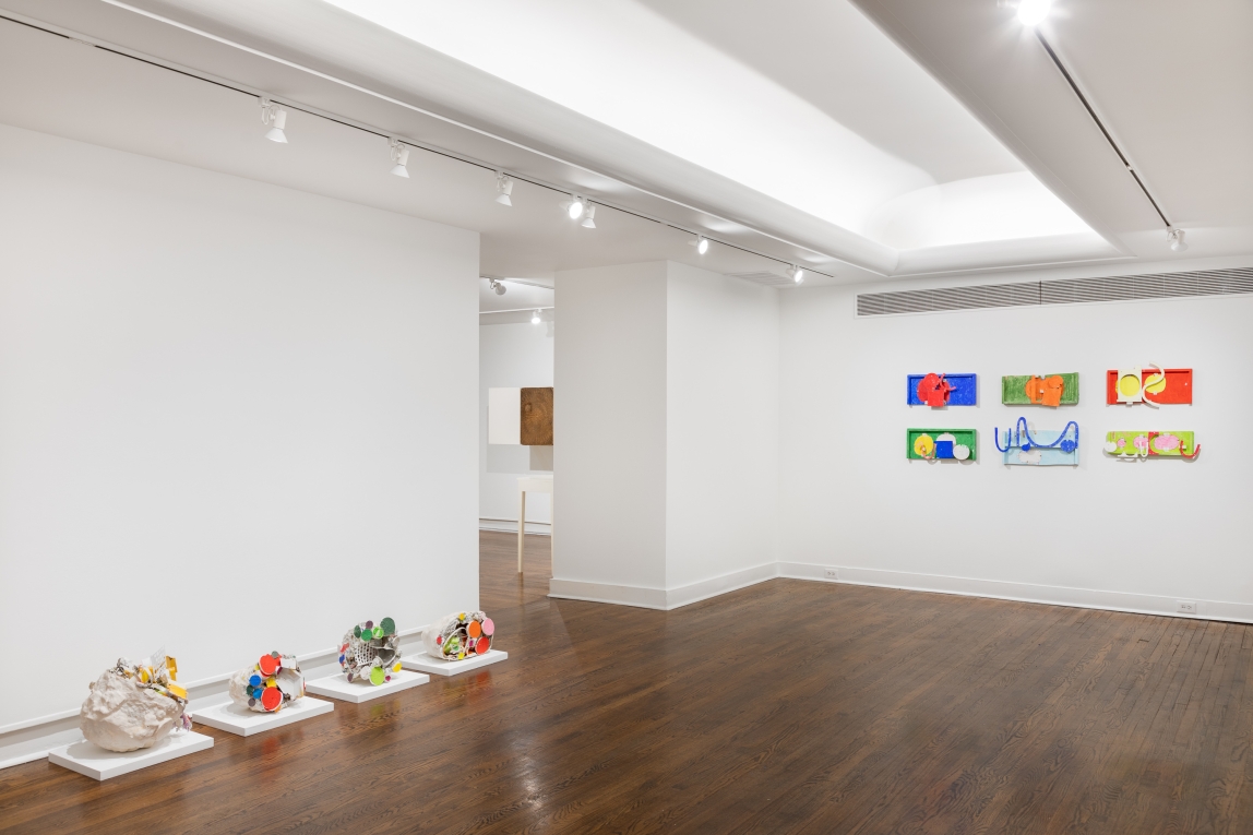 Installation view of four floor sculptures to the left and six colorful flat wood sculptures on the back wall to the right