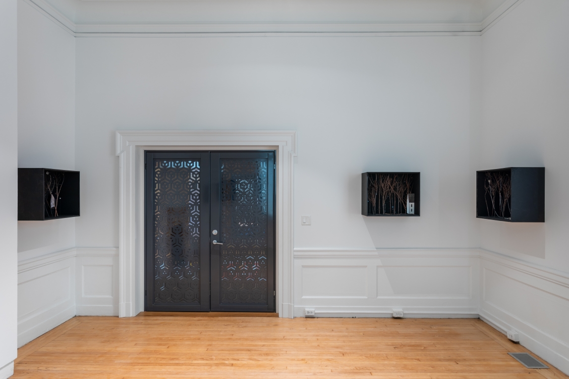 Installation view of three dioramas hanging in a row across three walls-two on facing walls, one on the back wall next to metal doors