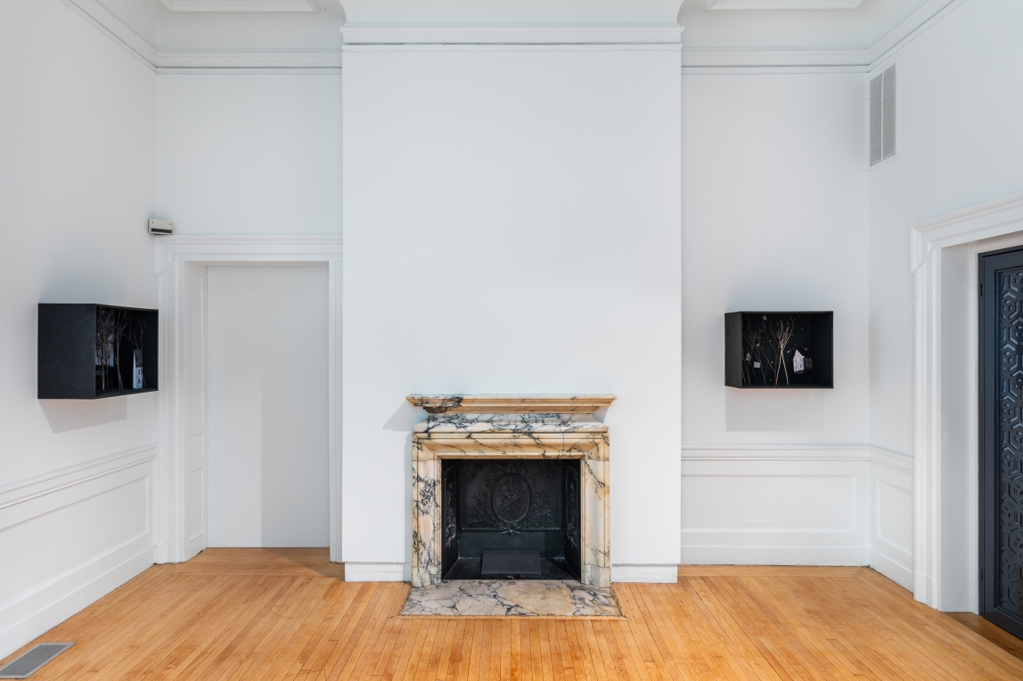 Installation view of two dioramas hanging on two different walls, with a fireplace in the center