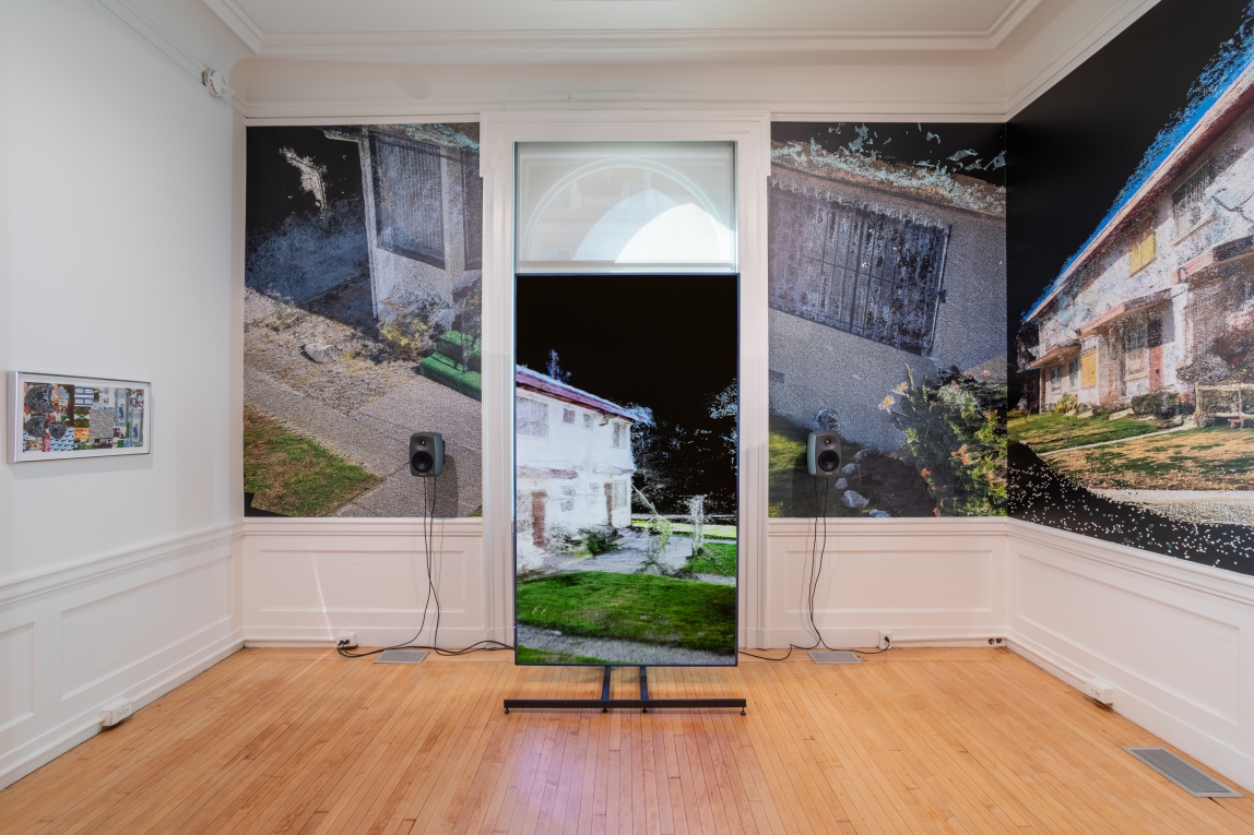 Installation view of large monitor with a film still of a house displayed, against wall with film still wallpaper