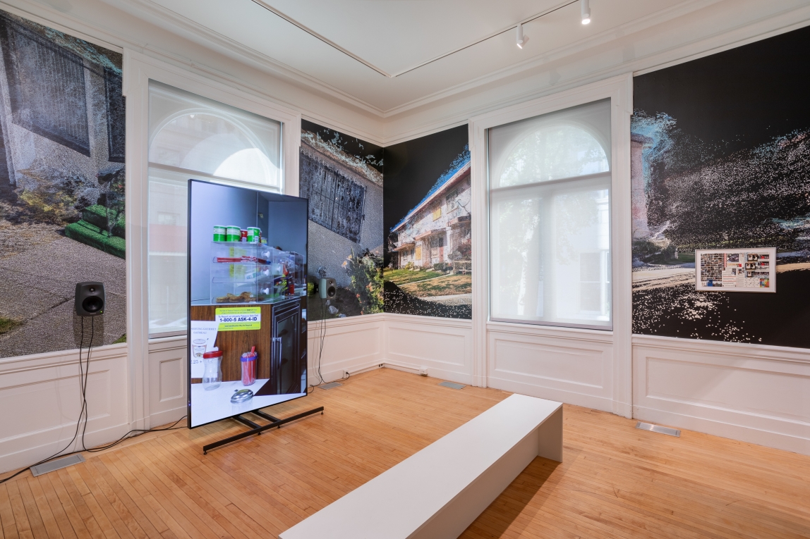 Installation view of large monitor to left with film still of store counter and a framed collage on wall to right with film still wallpaper behind
