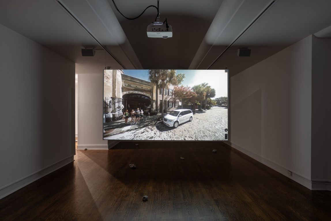 Installation view of projection in gallery depicting film still of a street