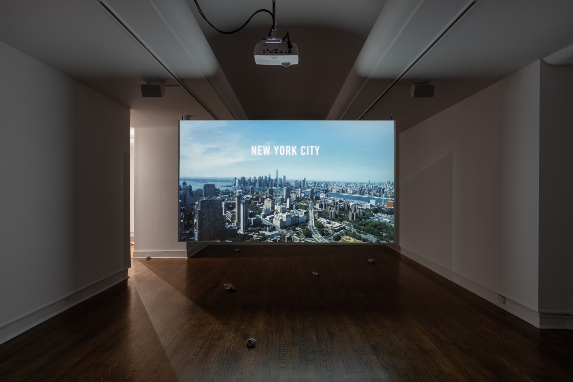 Installation view of film projected in gallery depicting an aerial view of New York City
