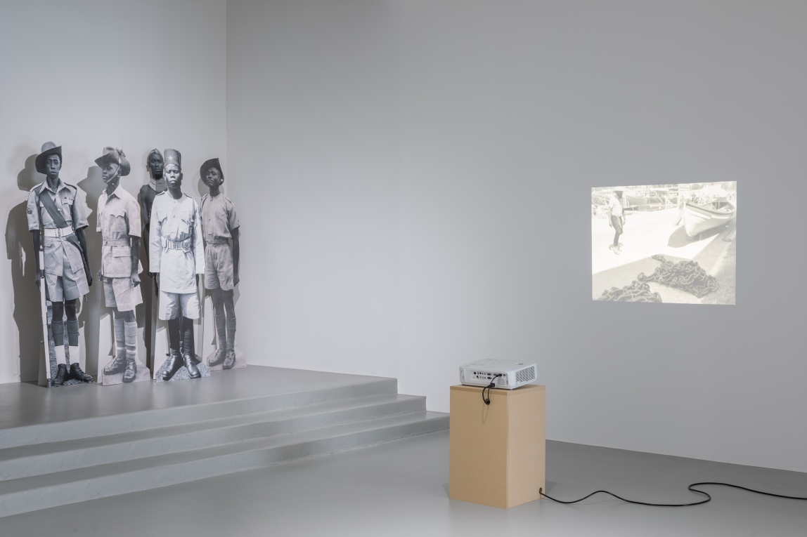 Installation view of projection on wall and a group of cardboard cutouts depicting Black soldiers