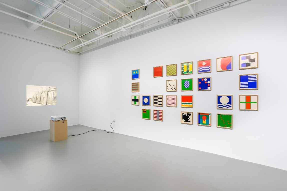Installation view of projection onto wall to left and framed squares of geometric patterns to the right