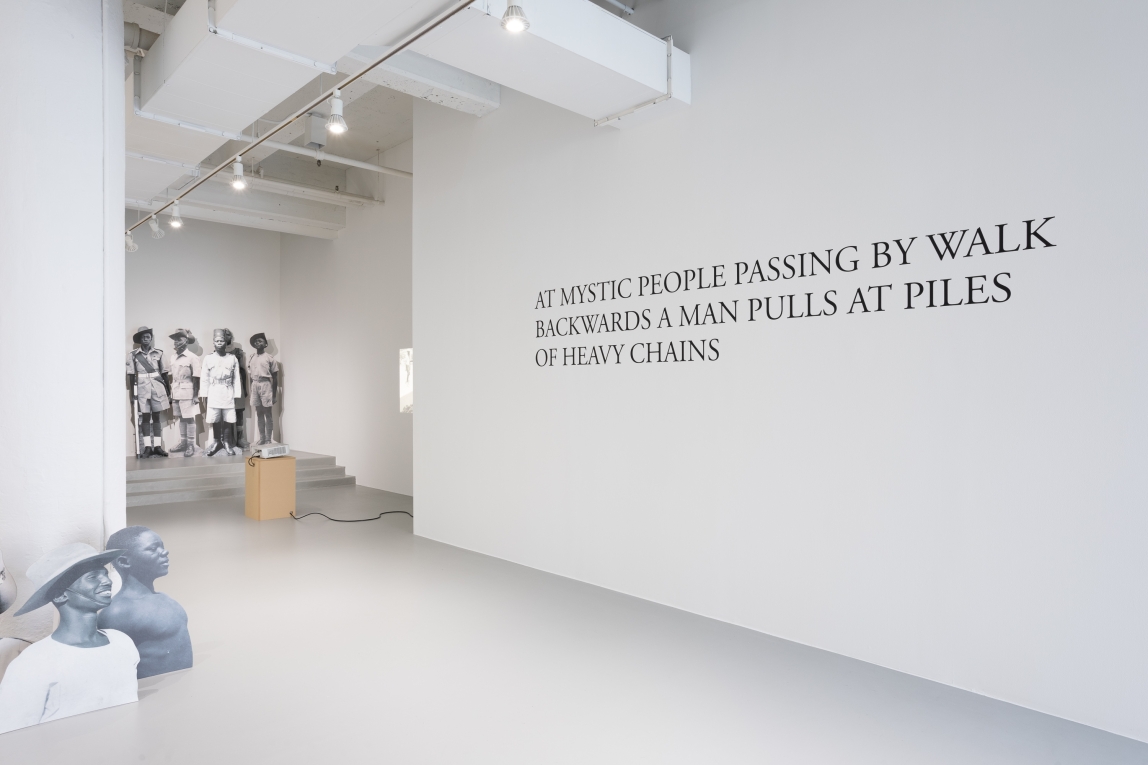 Installation view of  large text on wall and groupings of cardboard cutouts depicting Black soldiers throughout