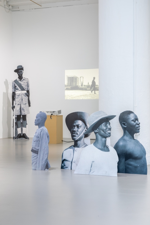 Installation view of projection on back wall and cardboard cutouts of Black soldiers in foreground and to the side