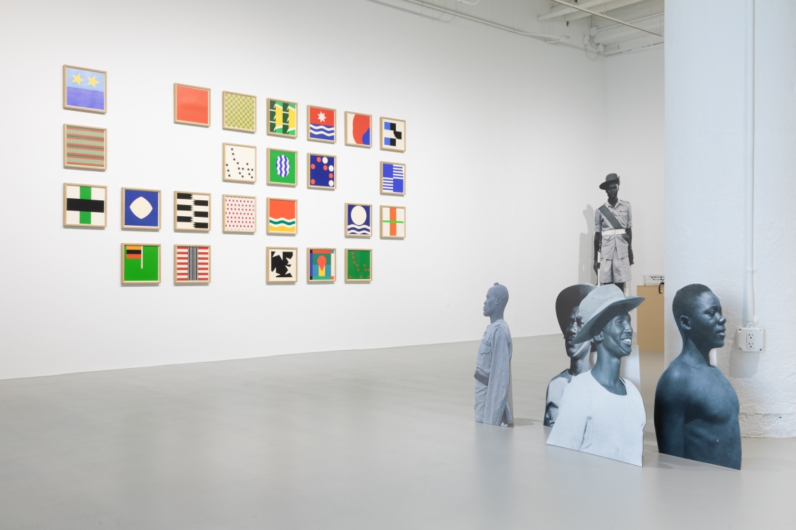 installation view of framed geometric squares on wall and cardboard cutouts depicting Black soldiers in foreground