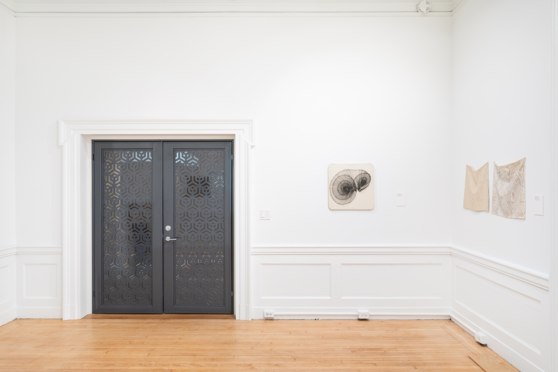 Installation view of Gallery A with three things hanging on the wall next to metal doors