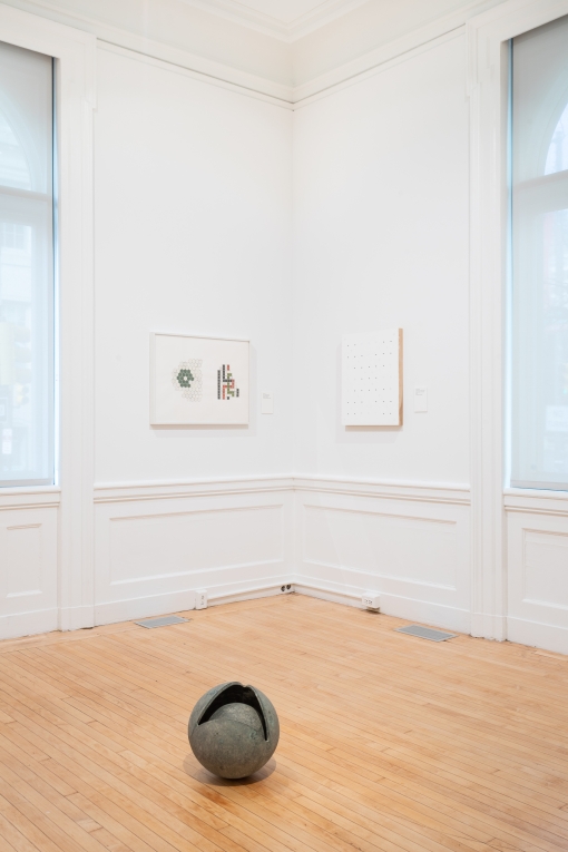 Installation view of corner of gallery with two works hanging on adjoining wall and sculpture on ground